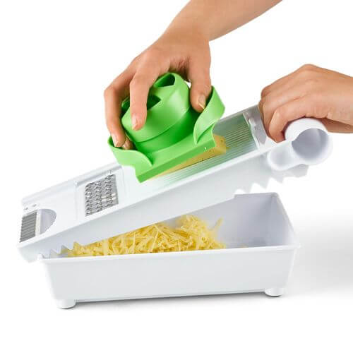 Vinsani 6 In 1 Grater Green & White being used to slice cheese with a safety holder, showcasing versatility in food preparation.