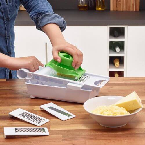 Vinsani 6 In 1 Grater Green & White being used to slice cheese on a wooden kitchen countertop.