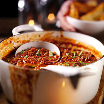 A delicious bowl of The Ultimate Beef Chilli with herbs, surrounded by warm ambiance.
